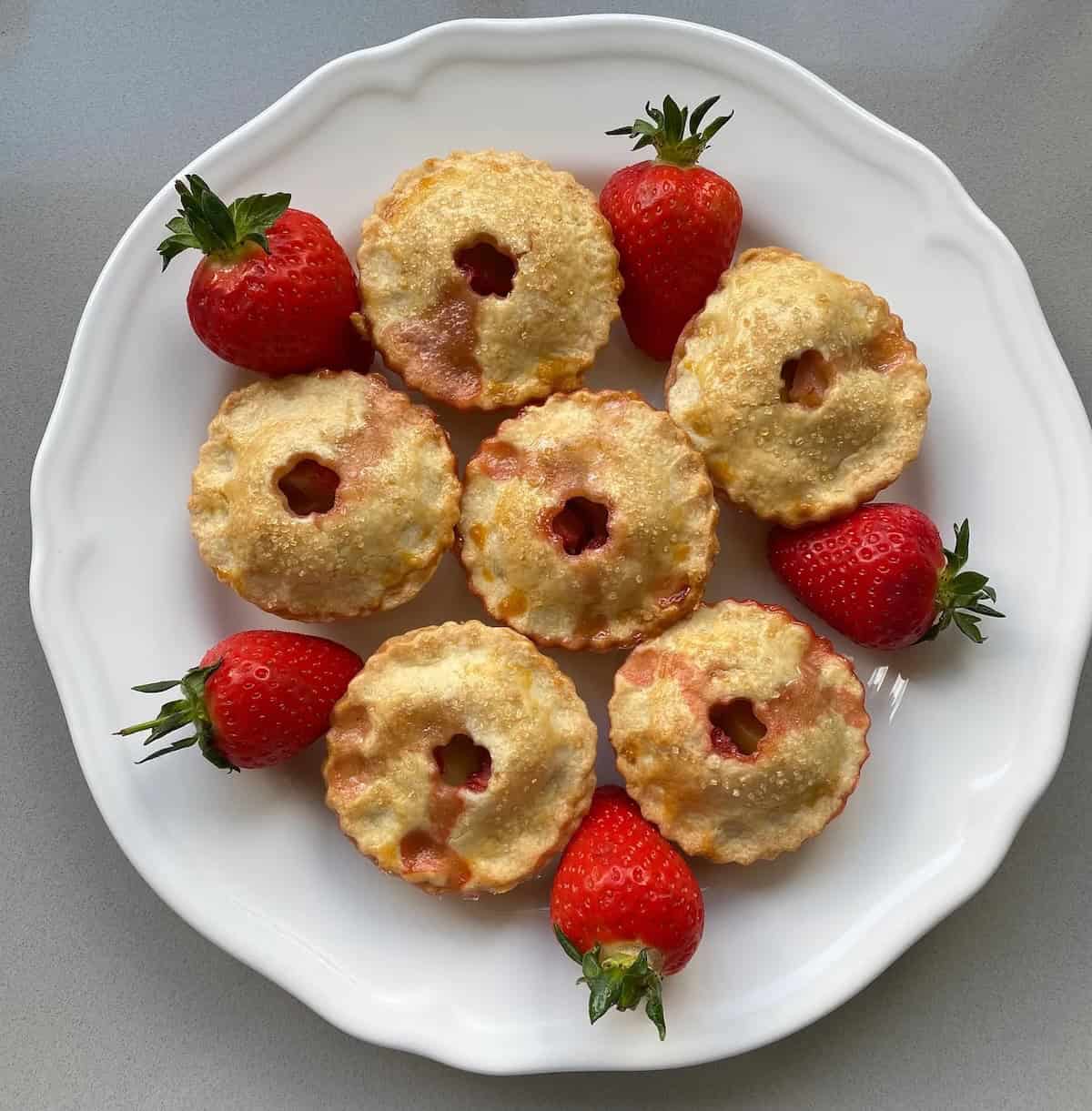 six fruit pies on a large plate. Plate of small apple and strawberry pies.