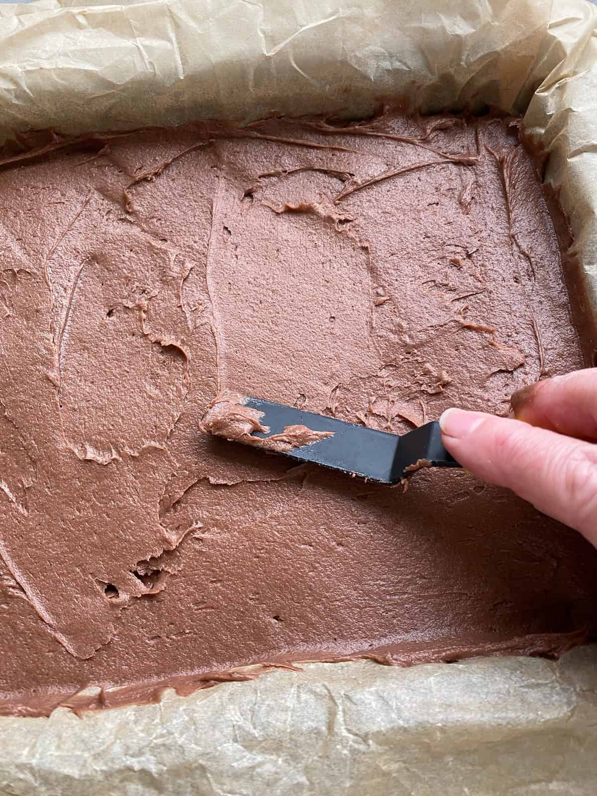 Spreading chocolate sponge mixture in a square baking tin.