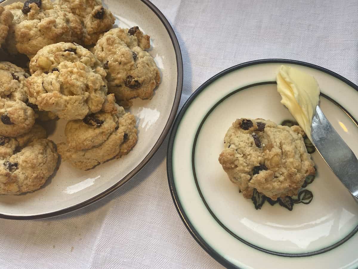 Rock Cakes (Rock Buns) on small plates with one on the side with a buttered knife.